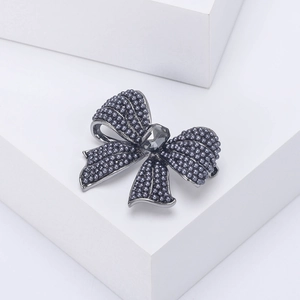 Macro detail of retro grey pearl bow brooch with a central rectangular crystal on a white step