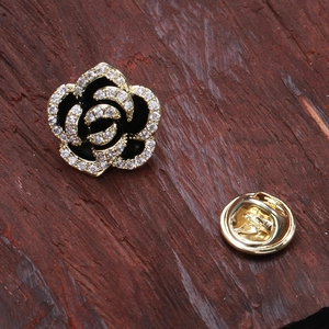 Macro detail of camellia brooch with black enamel, micro-set crystals and gold butterfly clasp