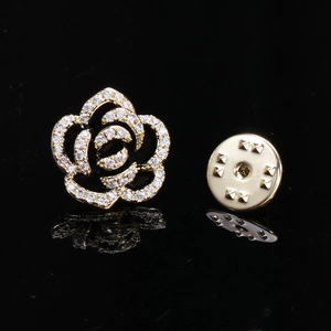 Elegant gold camellia flower brooch with cubic zirconia stones on reflective background