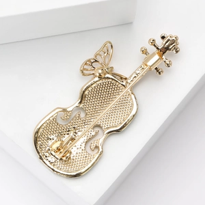 Broche violon plaquée or élégante avec papillon en émail sur un support blanc minimaliste