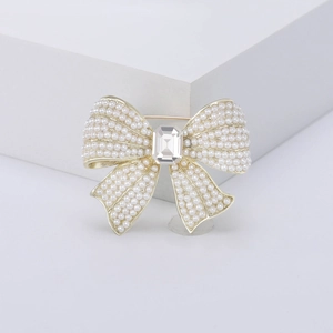 Elegant bow-shaped brooch with white pearls and emerald-cut crystal on a golden base