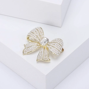 Detail shot of elegant bow brooch with white pearls and a square crystal on gold base