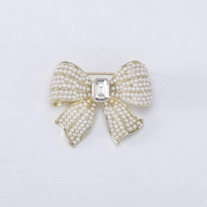 Detailed close-up of a gold bow brooch featuring inlaid pearls and a rectangular crystal