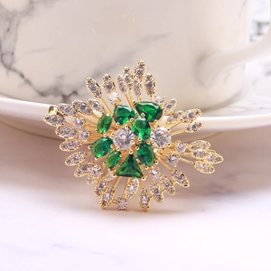 Macro detail of emerald green zircon brooch on marble background showing golden leaf patterns
