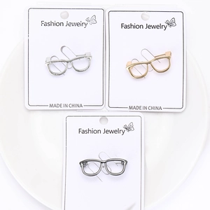 Detailed set of three glasses-shaped brooches in silver, gold, and grey on display cards