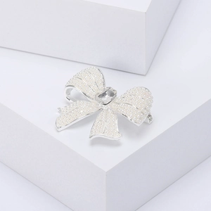 Detail of silver bow brooch with white pearls and a central crystal on white background
