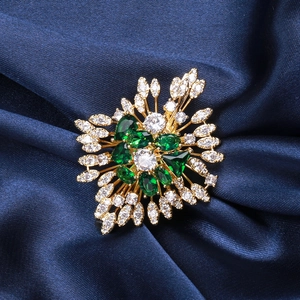 Close-up of luxury emerald green and white zircon flower brooch on dark blue satin fabric