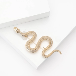 Elegant gold snake brooch with white crystals on a minimalist geometric white pedestal