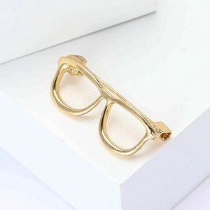 Minimalist gold-plated eyeglasses brooch pin displayed on a geometric prop