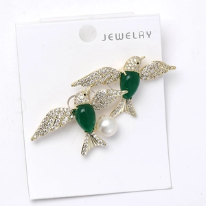 Detailed view of twin bird brooch with green zircon and white pearl on display card