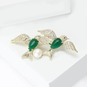 Elegant gold twin bird brooch featuring green gemstones, white pavé crystals and a pearl