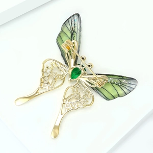 Detail view of gold butterfly brooch with green gemstone and intricate hollow wings