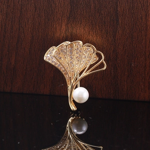 Makroaufnahme der goldenen Ginkgoblatt-Brosche mit Zirkonia-Steinen und weißer Perle