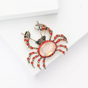 Close-up of alloy crab brooch with pink gemstone and red crystal inlay on white stand