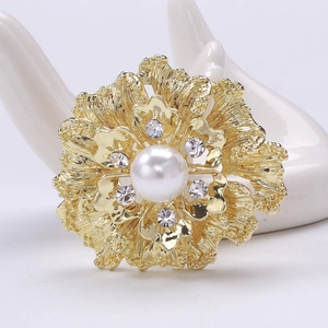 Detailed macro of golden flower brooch featuring centered pearl and sparkling rhinestones
