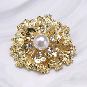 Close-up of golden floral brooch with a large white pearl and sparkling rhinestones