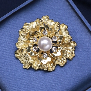 Detail of flower brooch with white pearl, rhinestones and golden textured petals
