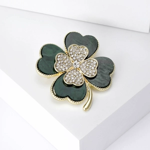 Detailed macro view of a green four-leaf clover brooch with gold plating and sparkling crystals