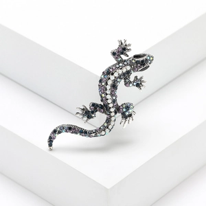 Close-up of gecko brooch with purple and blue crystals on a minimalist white stand