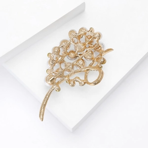 Detail view of golden leaf brooch with white pearl and green crystals on white background
