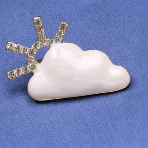 Macro detail of cloud brooch with white enamel, gold base and inlaid sparkling rhinestones