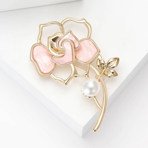 Détail de la broche fleur de camélia en émail rose avec cadre doré et perle blanche