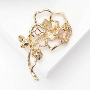 Élégante broche camélia en métal doré avec émail rose sur un piédestal blanc épuré