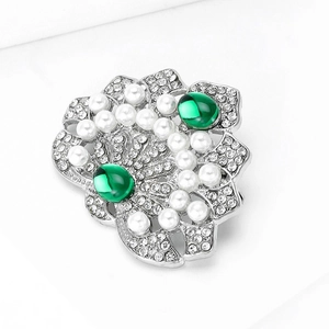 Détail d'une broche couronne de luxe avec pierres vertes, perles blanches et métal argenté
