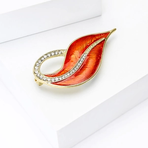 Detailed macro view of an elegant leaf brooch with orange enamel and sparkling crystals