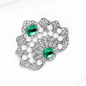 Détail d'une broche couronne de luxe avec pierres vert émeraude et perles sur métal