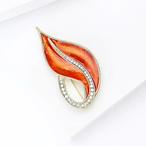 Close-up of golden leaf brooch with orange enamel finish and crystal rhinestones