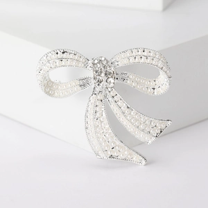 Macro detail of silver bow brooch with white pearls and sparkling crystal center