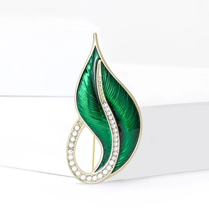 Elegant gold leaf brooch with green enamel and white crystals on white background