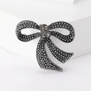 Vintage gunmetal bow brooch with grey pearls and clear rhinestones on white background