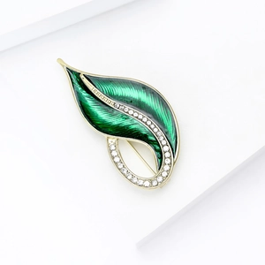 Close-up of elegant leaf brooch with green enamel, gold edges and crystal inlay
