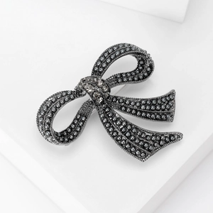 Detailed view of vintage grey pearl bow brooch with rhinestone center on white stand