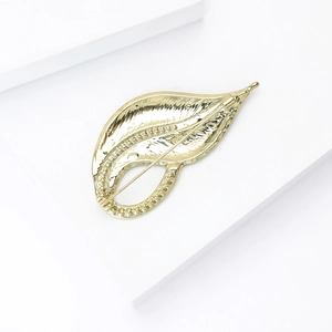 Detailed macro view of golden leaf enamel brooch with delicate texture on white display