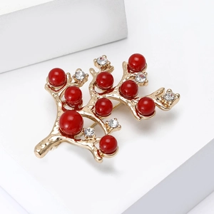 Vue détaillée d'une broche branche dorée avec perles rouges et strass étincelants