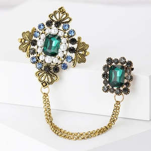Detailed close-up of vintage baroque double brooch with green stones and gold chains