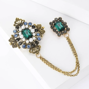 Macro detail of Baroque brooch with emerald crystal, pearls and gold twin chains
