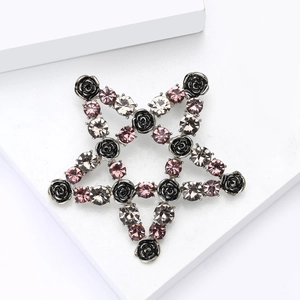 Detail of star-shaped brooch with black roses and pink crystals on geometric stand