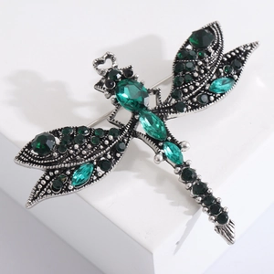 Macro shot of vintage dragonfly brooch with green emerald gemstones and silver metal finish