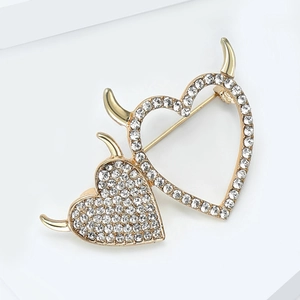 Detailed close-up of golden heart brooch with devil horns and sparkling rhinestones