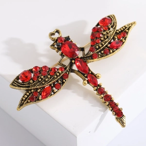Vintage gold dragonfly brooch with red rhinestones on a white geometric display stand
