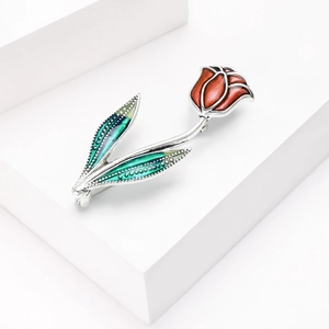 Détail d'une broche tulipe avec pétales en émail rouge et feuilles vertes sur support