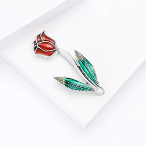 Détail macro d'une broche tulipe rouge avec feuilles vertes et monture en métal argenté