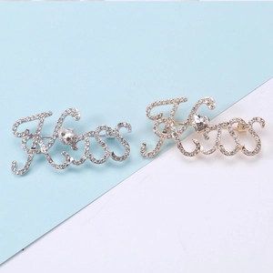 Dettaglio di spille con lettere Kiss e strass bianchi in finiture oro e argento
