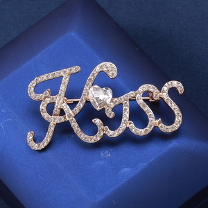 Dettaglio della spilla KISS dorata con strass scintillanti e una gemma a forma di cuore