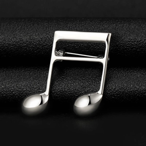 Macro detail of polished silver music note brooch on a textured black background