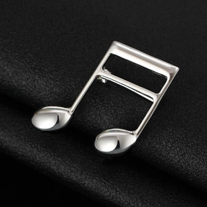 Close-up of polished silver musical note brooch on a premium black leather background